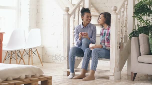Duas meninas afro-americanas encaracoladas se sentam nas escadas se divertem rindo e conversando juntas em casa — Vídeo de Stock