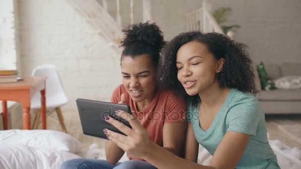 Dos chicas divertidas jóvenes de raza mixta hablando en skype en una tableta con sus padres en casa — Vídeo de stock