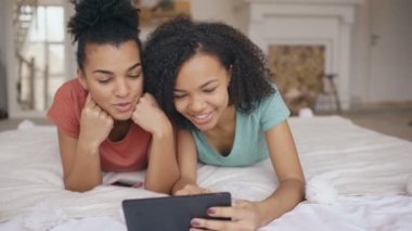 Tablet bilgisayar ve evde yatakta yatan görüşmeler kullanarak sosyal medya paylaşımı iki neşeli karışık yarış komik kız