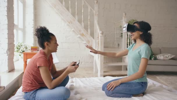 Mixed raste eine Frau mit Virtual-Reality-Brille, während ihr Freund einen digitalen Tablet-Computer in der Hand hielt. Freundinnen spielen Videospiel 3D-Technologie-Konzept zu Hause — Stockvideo