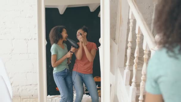 Gemengd ras grappige meisjes dansen zingen met haardroger en kam voor spiegel. Zusters plezier ontspanning in slaapkamer op home concept — Stockvideo