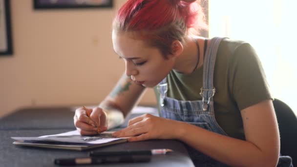 Vértes vonzó fiatal vörös hajú nő tetováló művész asztalnál ül, és vázlatot tetoválás stúdió beltéri létrehozása — Stock videók
