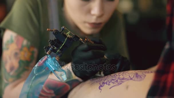 Close-up de jovem tatuagem de cabelos vermelhos artista mulher tatuagem imagem na perna do cliente sobre esboço em estúdio dentro de casa — Vídeo de Stock