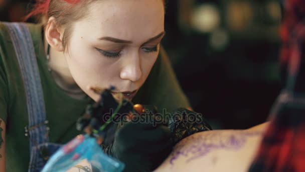 Primo piano della giovane donna tatuatrice dai capelli rossi tatuando l'immagine sulla gamba del cliente sopra lo schizzo in studio al chiuso — Video Stock