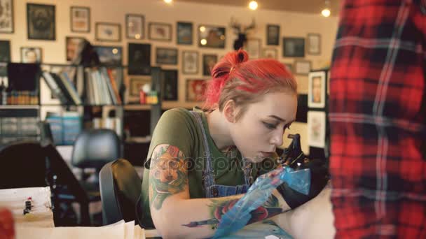 Bella donna dai capelli rossi tatuaggio artista tatuaggio foto sulla gamba di giovane ragazza client in studio — Video Stock