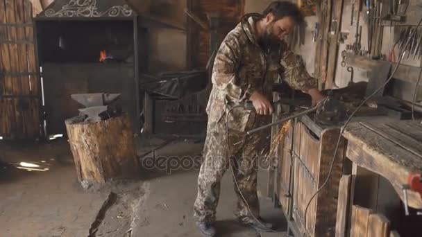 Brodaty młody człowiek szlifierką kątową do pracy na kawałek metalu w warsztacie kowala, szlifowanie iskry latają — Wideo stockowe