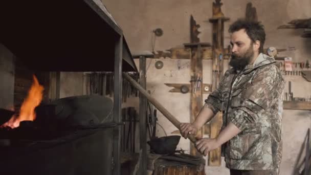 Bebaarde man smid branden originele forge haard met lucht bij historische smithy binnenshuis — Stockvideo