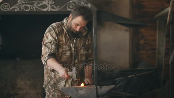 Bearded young man blacksmith manually forging hot metal on the anvil in smithy with spark fireworks — Stock Video