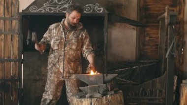 Sakallı genç adam demirci el ile sıcak metal smithy kıvılcım havai fişek ile örs üzerinde dövme Slowmotion