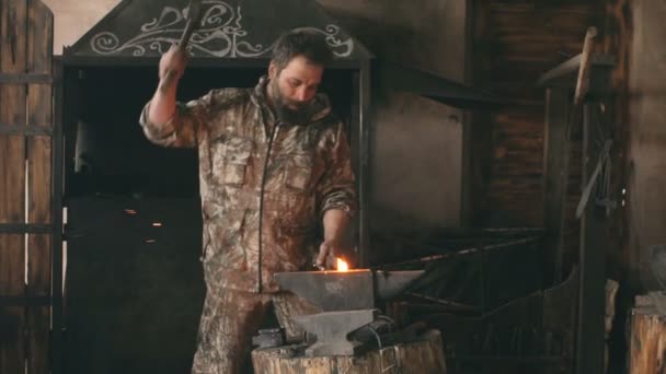 Slowmotion del herrero joven barbudo forjando manualmente metal caliente en el yunque en herrería con fuegos artificiales de chispa — Vídeo de stock