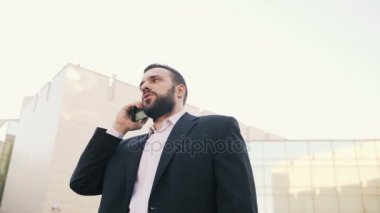 Düşük açılı ve dolly anlaşmalar yapmaya cep telefonuyla konuşan iş adam, vurdu ve modern ofis binaları stand