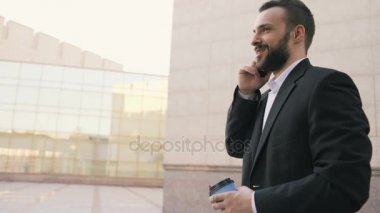 Dolly atış smartphone ile kahve yakınındaki modern ofis binaları, konuşan genç sakallı iş adam