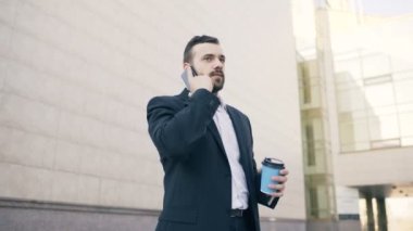 Smartphone ile kahve yakınındaki modern ofis binaları, konuşan genç sakallı iş adam düşük açılı çekim