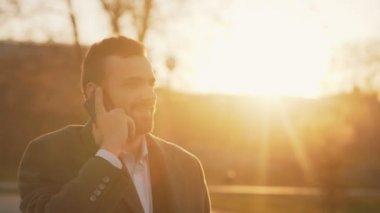 Portre genç iş adamı smartphone vasıl konuşuyor ve akşam saat içinde güneş ışığı arkadan aydınlatmalı yoIda fırsatlar yapma paltolu sakallı
