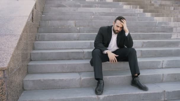 Joven hombre de negocios molesto teniendo estrés y sentado en las escaleras en la calle. Empresario que tiene el concepto de problemas de reparto — Vídeo de stock