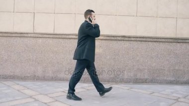 Dolly smartphone ve hissediyor yürüyüşler anlaşma yapma konusunda mutlu konuşan genç sakallı iş adam çekim yakınındaki ofis binaları