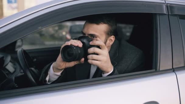 Jonge prive-detective man zit in de auto en fotograferen met dslr camera — Stockvideo