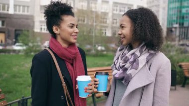 İki çekici karışık yarış kadınla poşetler kahve içme ve sokağın konuşuyor. Genç kız gülümseyerek ve arkadaş sohbet