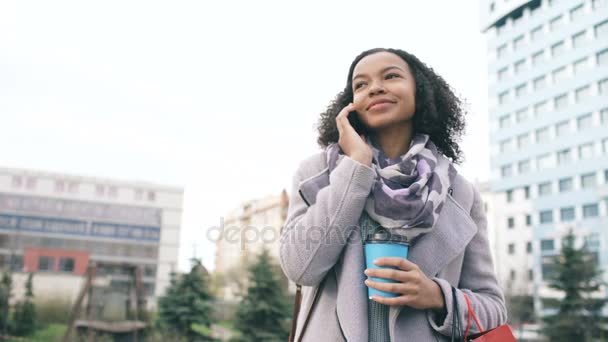 Attraente mista ragazza gara parlando smartphone e bere caffè in strada con le borse. Giovane donna dopo lo shopping in vendita centro commerciale — Video Stock