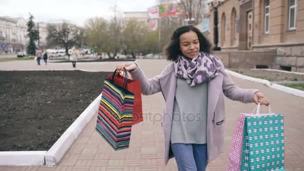 Dolly strzał atrakcyjne mieszanej rasy dziewczyna taniec i zabawy podczas spaceru na ulicy z torby. Szczęśliwa młoda kobieta, chodzenie po zakupy na sprzedaż centrum — Wideo stockowe