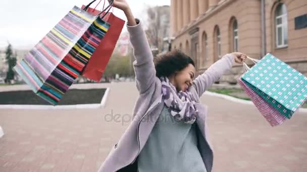 Vonzó vegyes verseny lány táncolni és szórakozni, miközben az utcán táskákkal. Boldog fiatal nő gyaloglás után shopping mall eladó — Stock videók