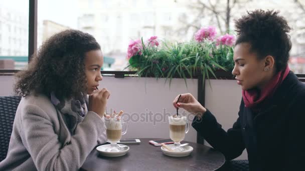 Två attraktiva blandad ras kvinnor prata och dricka kaffe i gatan café. Vänner har roligt efter att ha besökt mall försäljning — Stockvideo