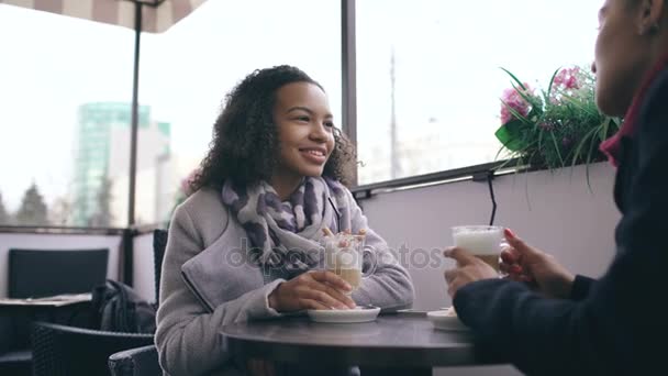 Twee aantrekkelijke gemengd ras vrouwen praten en drinken koffie in straat café. Vrienden hebben plezier na een bezoek aan winkelcentrum verkoop — Stockvideo