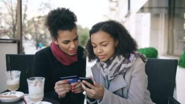 Online Kredi kartı ve smartphone ile konuşmak ve sokak kafede kahve içme sırasında alışveriş sahip iki çekici karışık yarış bayanlar