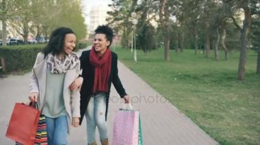 İki çekici karışık yarış bayanlar dans çekim dolly ve eğlenceli alışveriş torbaları ile park aşağı yürürken. Alışveriş Merkezi satış ziyaret ettikten sonra mutlu genç arkadaş yürüyüş