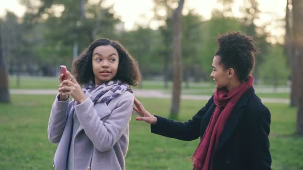 Дві привабливі змішані раси жінки зненацька зустрічаються в парку біля торгового центру — стокове відео