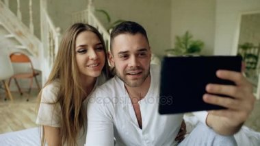 Tablet bilgisayar holding ve arkadaşlar evde yatakta oturmuş sohbet görüntülü sohbet sahip genç tatlı ve sevgi dolu Çift
