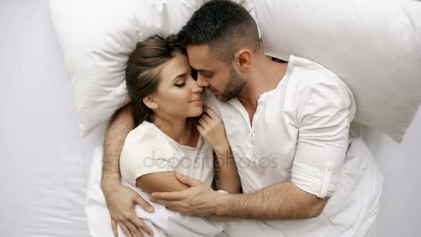 Joven pareja hermosa y cariñosa beso y abrazo en la cama mientras se despierta por la mañana. Vista superior de hombre atractivo besándose y hablando su esposa sonriente — Vídeos de Stock