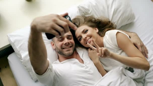 Jeune beau et aimant couple prendre selfie photo sur smartphone caméra et baiser tout couché dans le lit le matin — Video