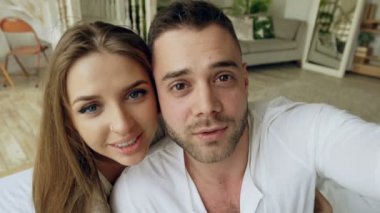 Genç tatlı tatlı ve sevgi dolu çift Smartphone holding ve arkadaşlar evde yatakta oturmuş sohbet görüntülü sohbet sahip