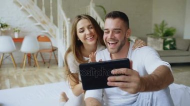 Tablet kullanan genç çekici adam gel anf ise onun girlfrined görüntülü sohbet sahip bilgisayar sarıl ona. Anne evde yatakta oturmuş sohbet tatlı sevgi dolu Çift