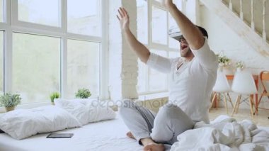 Evde yatakta otururken 360 Vr video deneyimi olan sanal gerçeklik kulaklık giyen genç neşeli adam