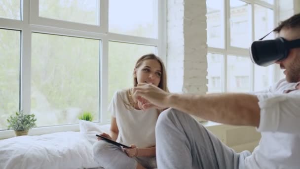 Fiatal aranyos pár, a tábla-PC és a virtuális-valóság sisak 360 Vr videó lejátszás game az ágyban otthon ülve — Stock videók
