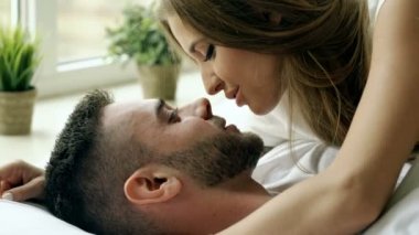 Genç gülümsemek güzel ve sevgi dolu bir çift oynamak ve sabah yatakta öp. Çekici bir adam karısını yatakta sarılma ve öpüşme