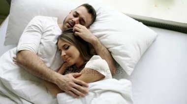Genç güzel ve sevgi dolu çift öpücük ve sabah uyanma sırasında yatağa sarıl. Çekici adam öpüşme ve gülümseyen karısı konuşmaya Üstten Görünüm