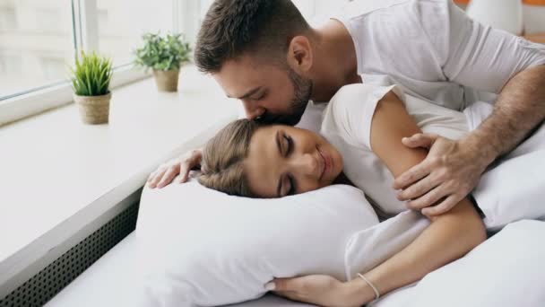 Unga vackra och kärleksfulla paret som vaknar på morgonen. Attraktiv man kyssa och krama sin fru i sängen — Stockvideo