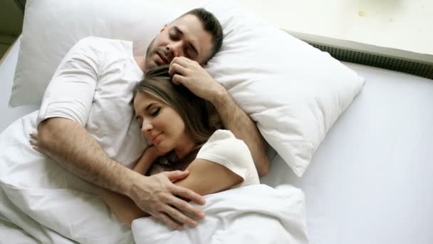 Молодая красивая и любящая пара целуется и обнимается в постели, просыпаясь утром. Вид сверху привлекательного мужчины, целующегося и разговаривающего со своей улыбающейся женой — стоковое видео
