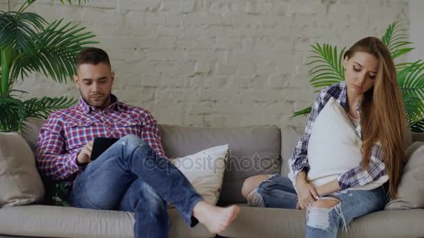 自宅のソファに座っている若い女性は彼氏のタブレット コンピューターを使用しながらストレスと不幸な動揺 — ストック動画