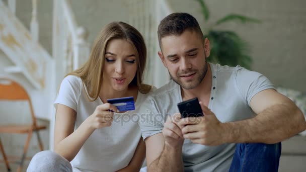 Casal jovem atraente com smartphone e cartão de crédito compras na internet sentar na cama em casa — Vídeo de Stock