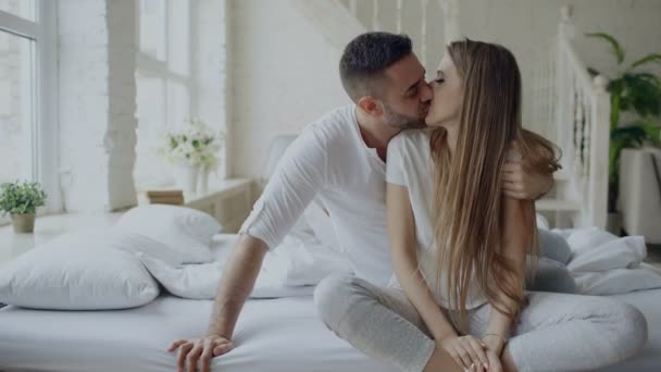 Young beautiful and loving couple embrace and kisisng while sitting on bed after waking up in the morning — Stock Video