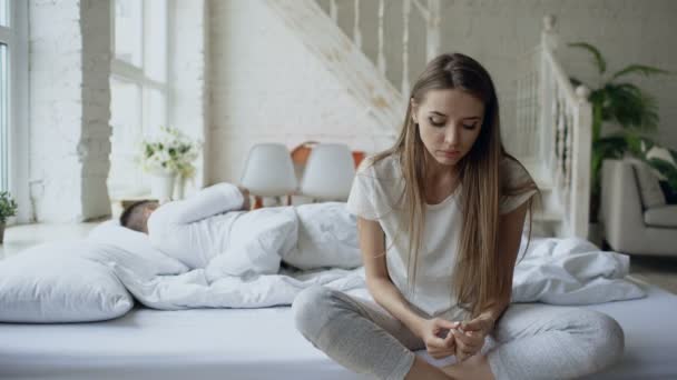 Depressive junge Frau sitzt im Bett und weint, während ihr Freund zu Hause im Bett liegt — Stockvideo