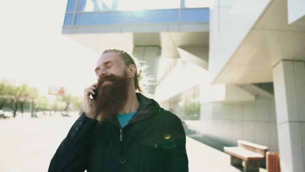 Joven barbudo hipster hombre concentrado hablando por teléfono en citystreet, conversación cerca de edificio de oficinas — Vídeos de Stock