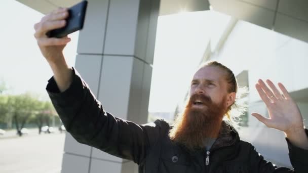 Young bebaarde hipster man selfie foto met behulp van smartphone camera buiten bij city straat — Stockvideo