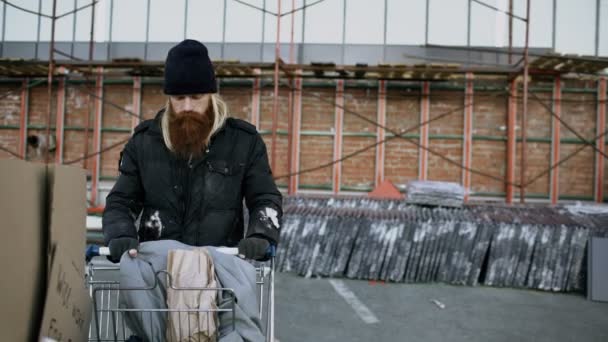 Dolly shot di barbuto senzatetto che cammina per strada con carta sparatoria nella fredda giornata autunnale — Video Stock