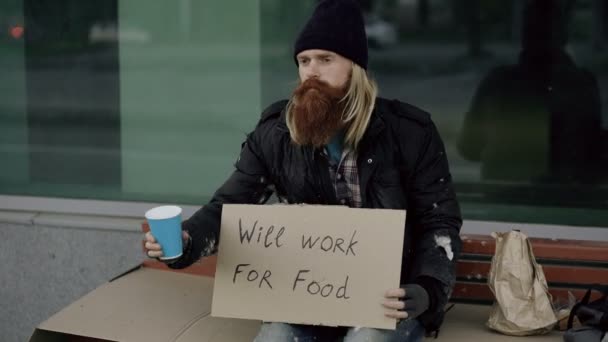 Obdachloser junger Mann bettelt um Geld schüttelt Tasse, um Aufmerksamkeit Menschen zu schenken, die in der Nähe Bettler auf dem Bürgersteig der Stadt gehen — Stockvideo