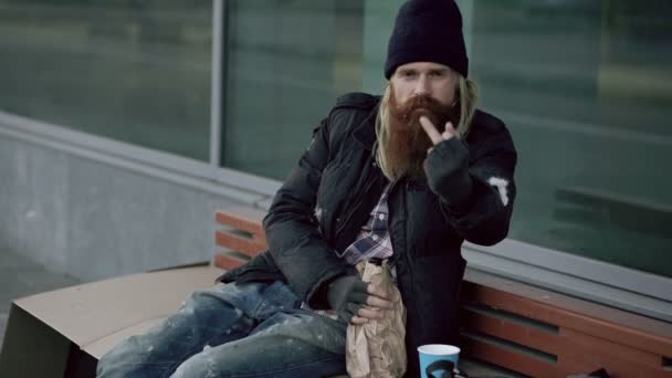 Дуже п'яний бездомний чоловік показує, як ти підписуєшся в камеру і спить, сидячи на лавці на тротуарі — стокове відео